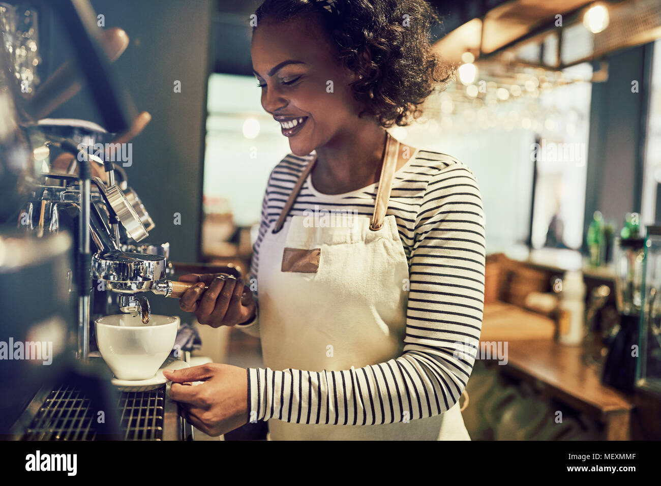 Smiling young African barista de préparer une tasse de café tout en se tenant à un café dans un café branché Banque D'Images