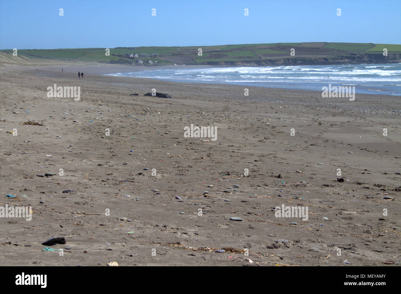 Couple en train de marcher sur une plage de sable vide par un beau jour d'été avec les vagues en roulant sur une brise de mer. Owenahincha beach l'Irlande. Banque D'Images