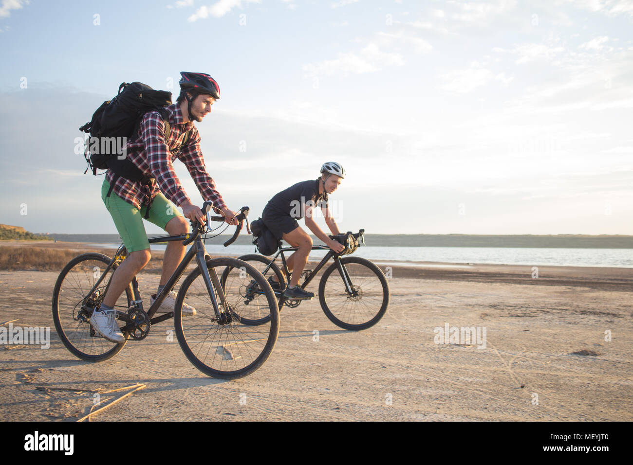 Deux jeunes hommes sur un vélos de cyclotourisme avec des sacs et casques dans le désert sur un voyage en vélo, amis'avoir in sunny day Banque D'Images