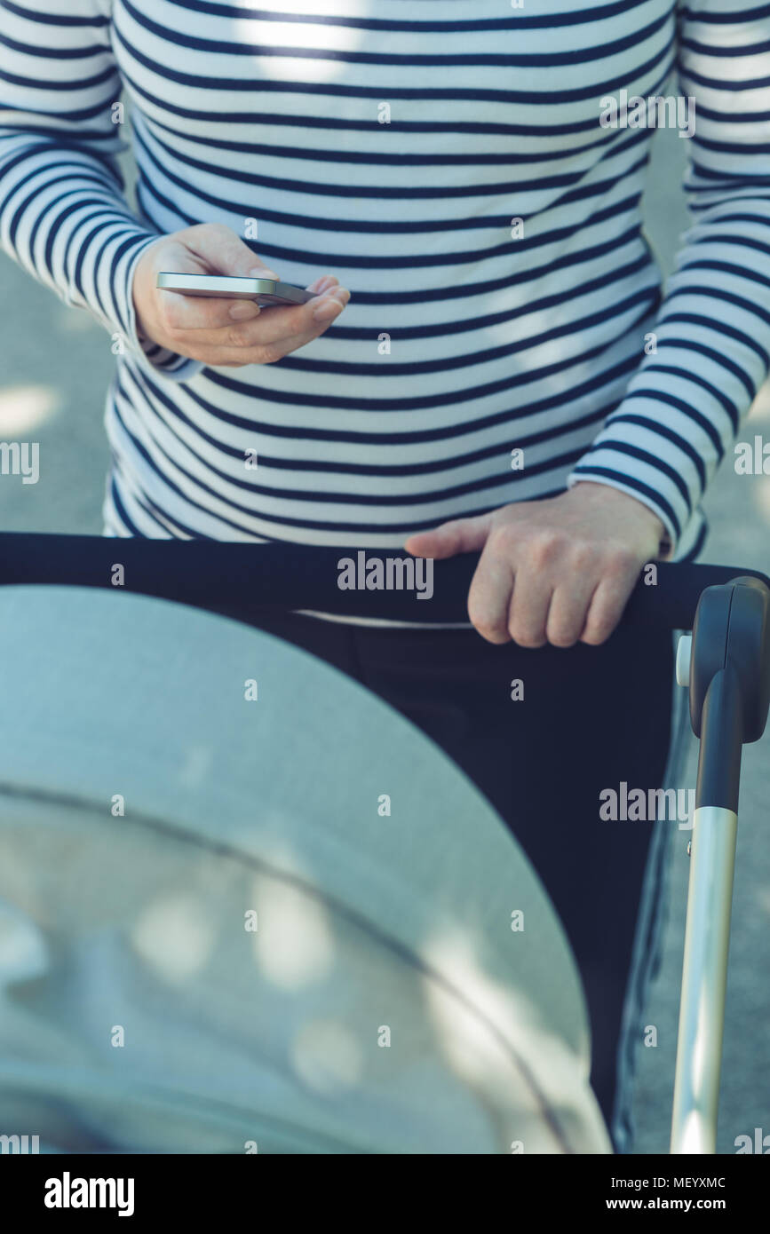 Mère à l'aide de téléphone mobile tout en poussant la poussette de bébé dans la rue, selective focus Banque D'Images