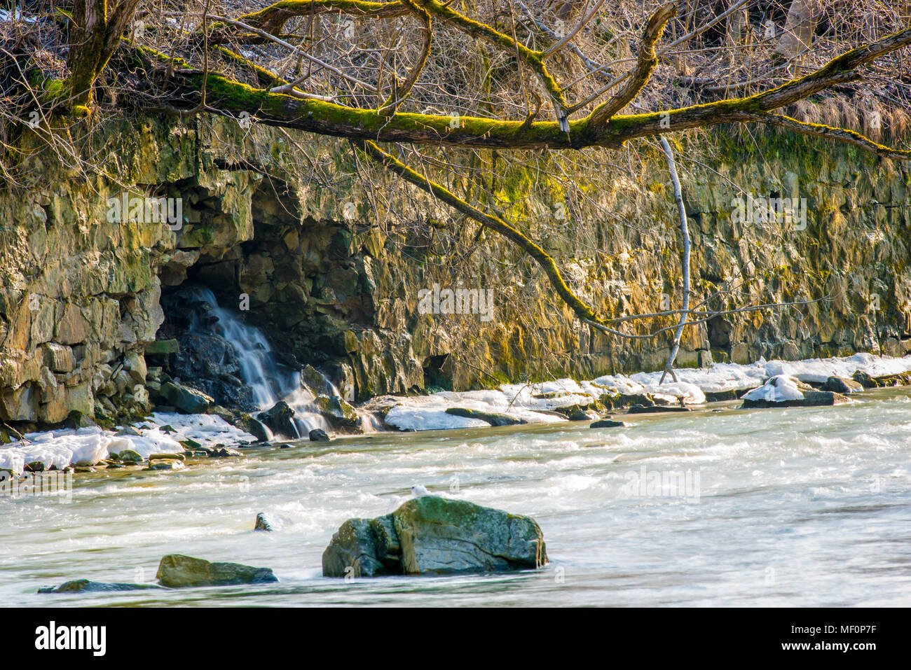 Mur de montagnes Rocheuses par la rivière avec chute d'eau venant de la grotte cachée Banque D'Images