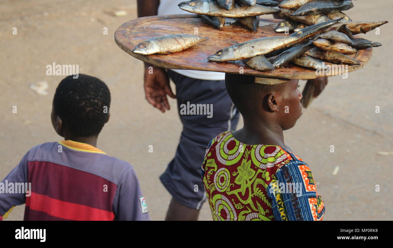 Homme africain en vêtements traditionnels un étui pour le bac de poisson séché sur sa tête, Close up, Elmina, Ghana Banque D'Images