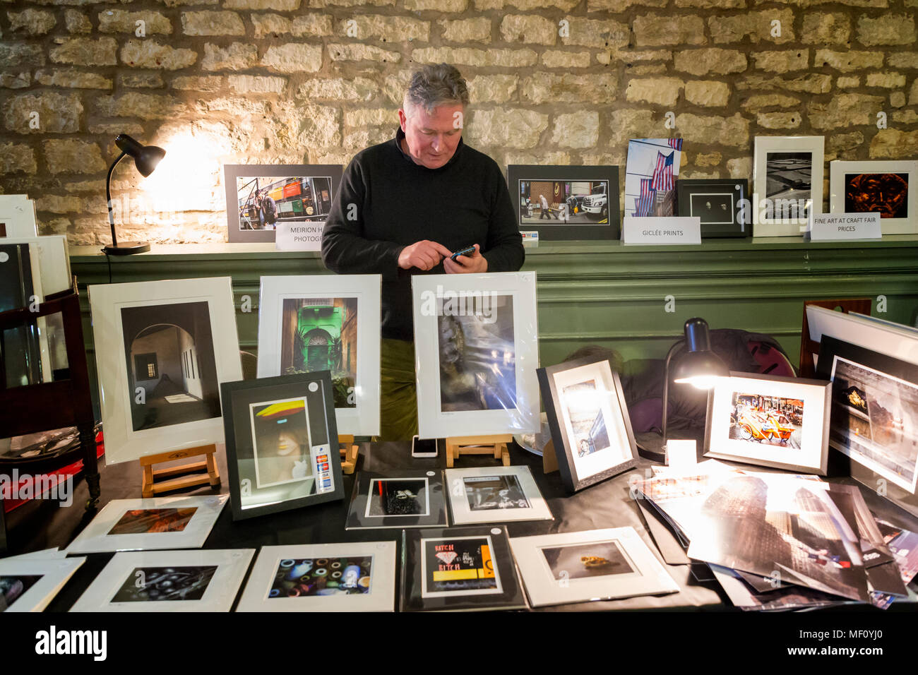 Contrôle de sa calculatrice photographe derrière ses images encadrées sur un étal de Cirencester's Hall de maïs Banque D'Images