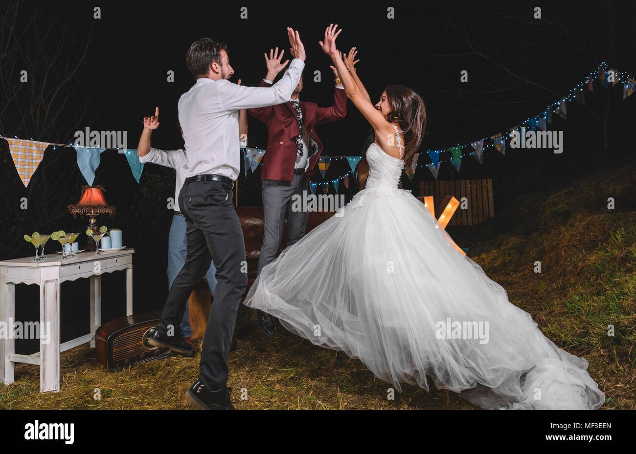 Happy bride saut et offrant un rapport cinq avec ses amis sur un champ de nuit fête entre amis Banque D'Images