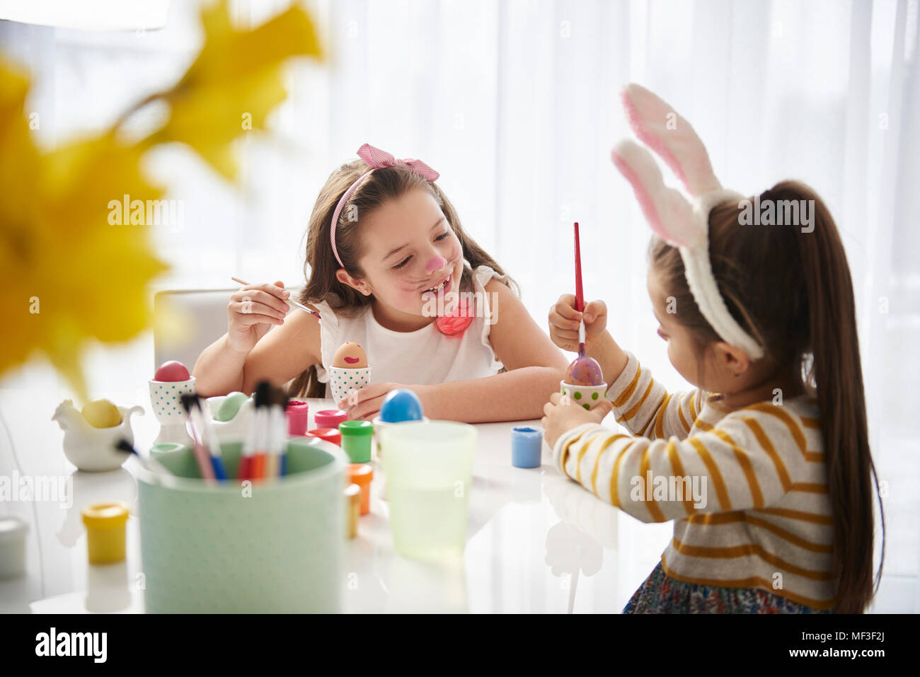 Sisters sitting at table painting Easter eggs Banque D'Images