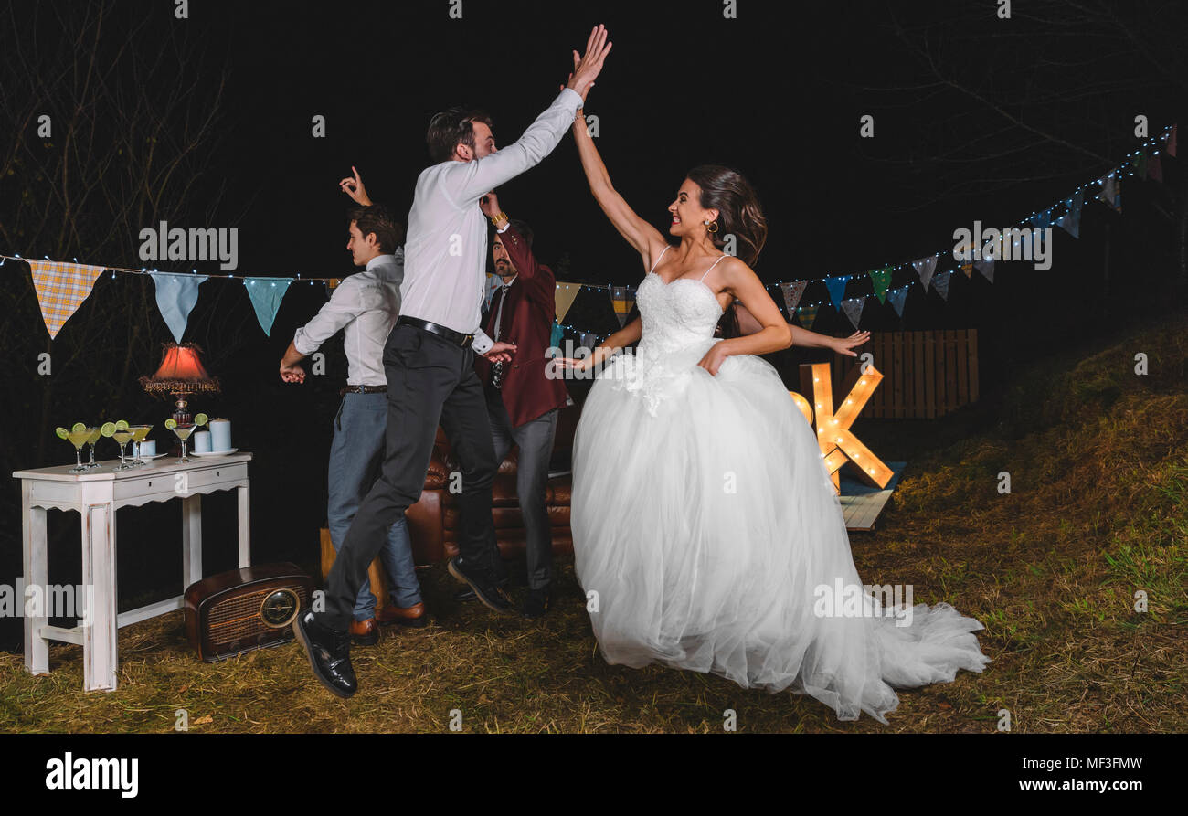 Happy bride saut et offrant un rapport cinq avec jeune homme sur un champ de nuit fête entre amis Banque D'Images