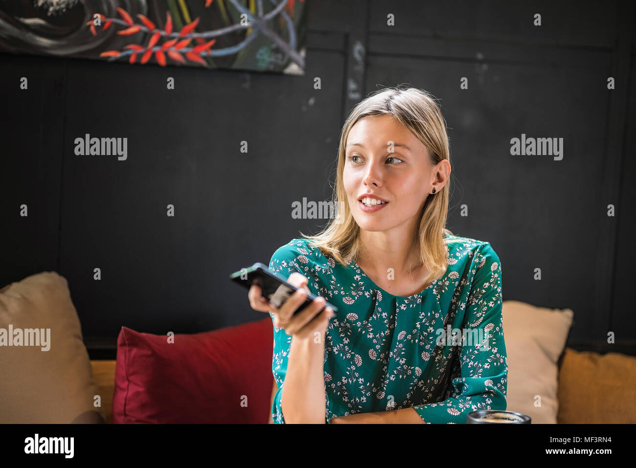 Young smiling woman with green dress sitting in cafe, tenant son smartphone Banque D'Images