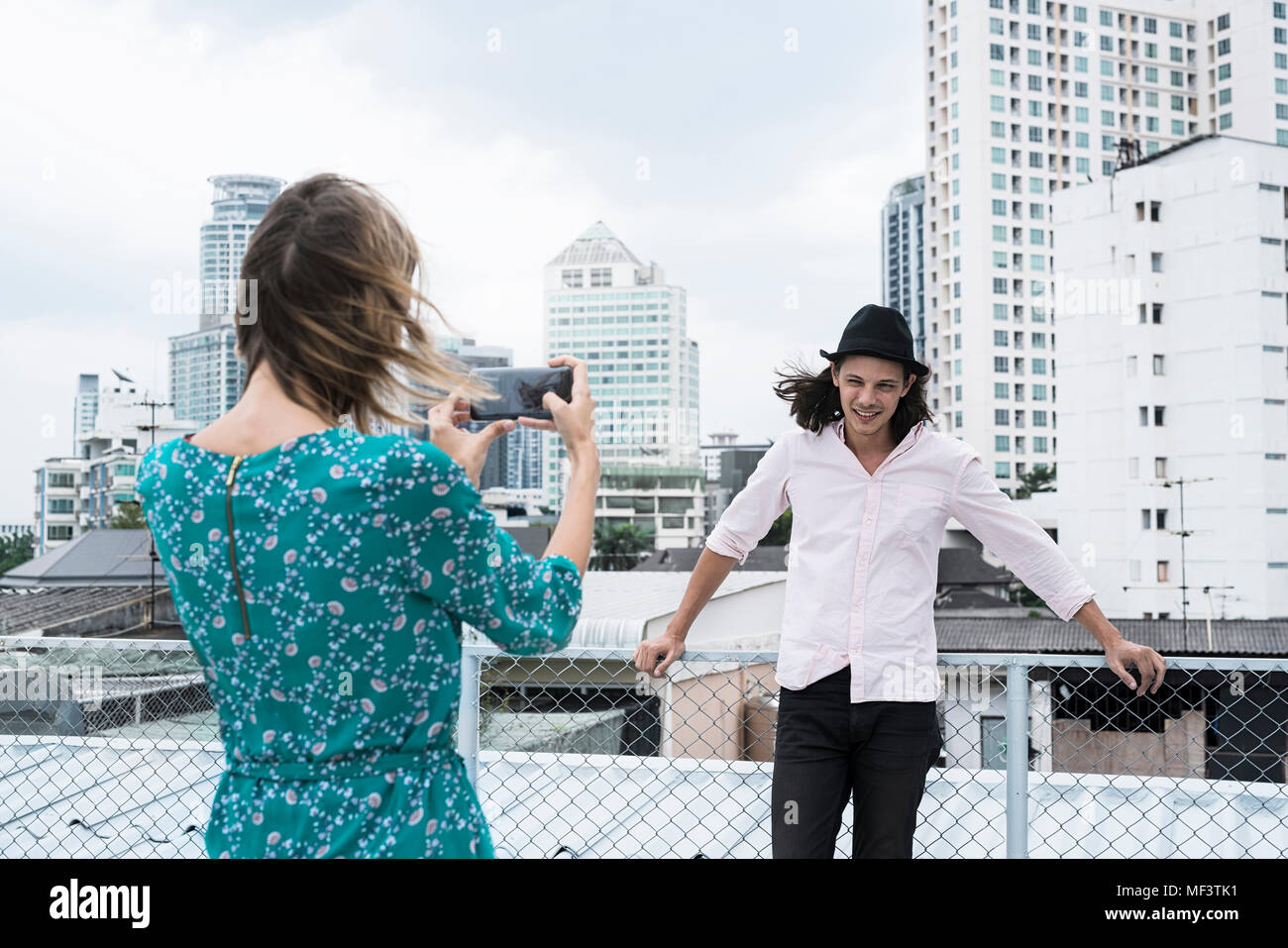 Young woman with smartphone taking picture of boyfriend on rooftop Banque D'Images