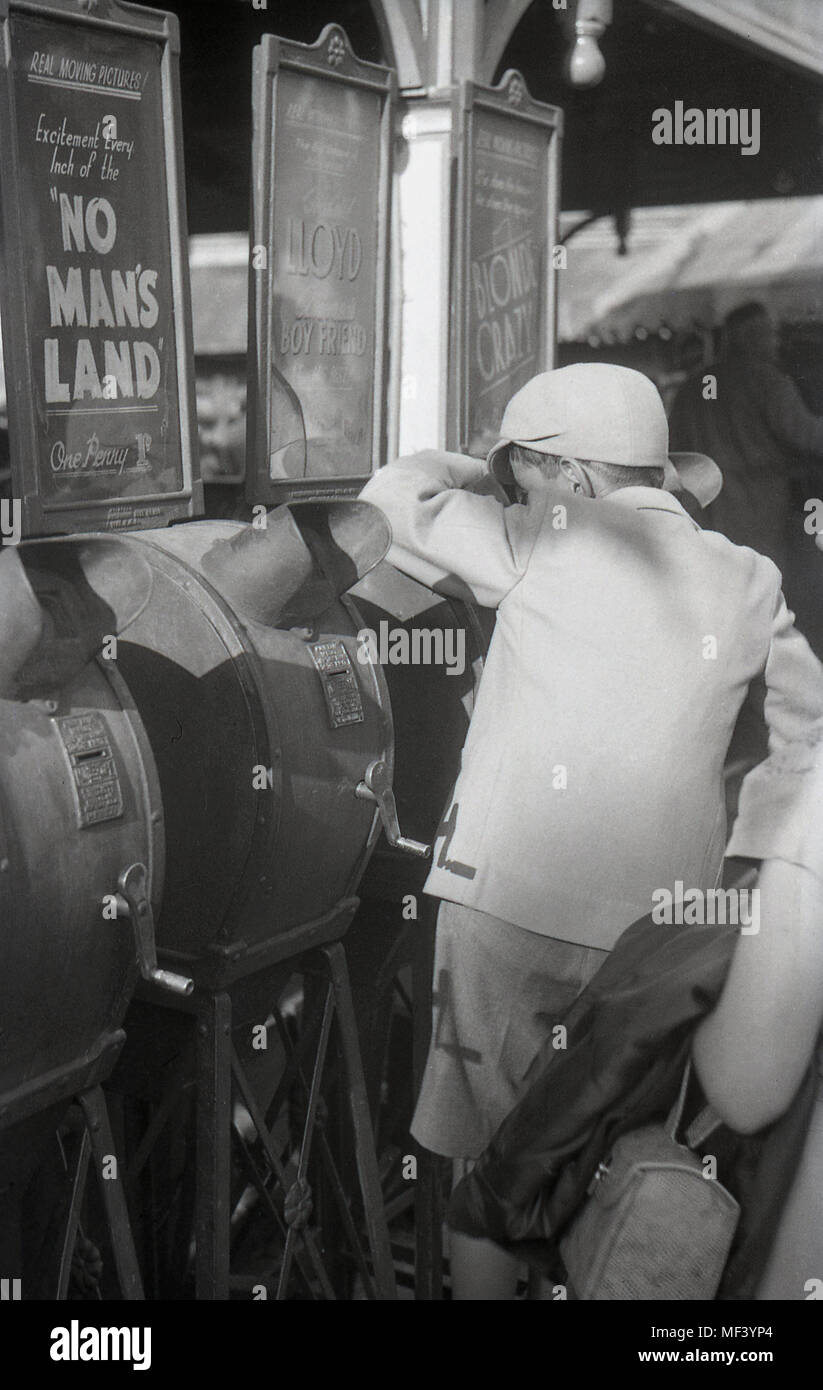1940, historiques, jeune écolier à l'aide d'un film d'arcade mutoscope viewer lors d'une fête foraine, Londres, Angleterre, Royaume-Uni. Ces machines fonctionnant avec des pièces figurant un rabatteur de carte photos encore que fliped donnant ainsi un film d'animation ou film. Banque D'Images