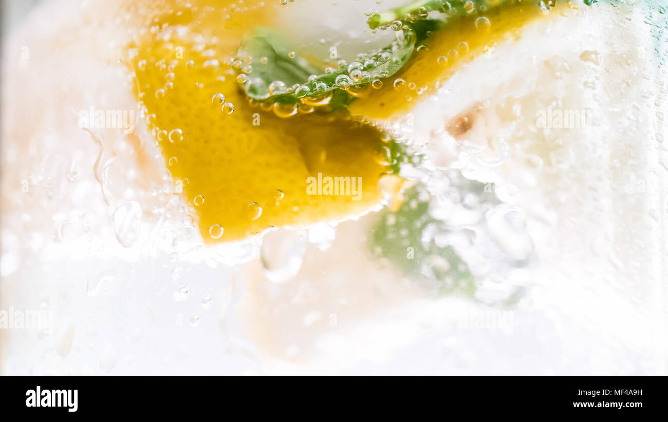 Macro photo de bulles d'air sur les feuilles de menthe et les rondelles de citron dans l'eau froide Banque D'Images