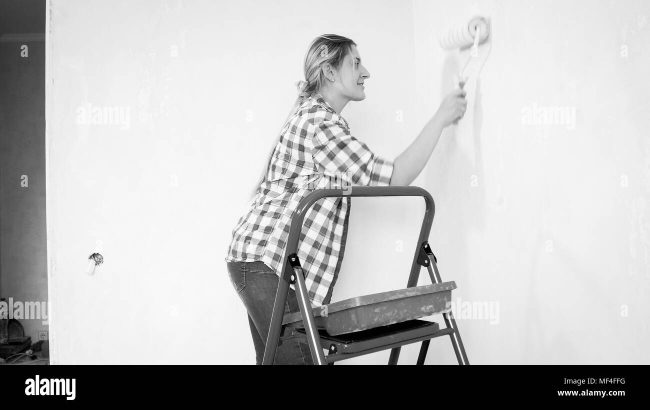 Image en noir et blanc de belle jeune femme peinture des murs avec rouleau à peindre Banque D'Images