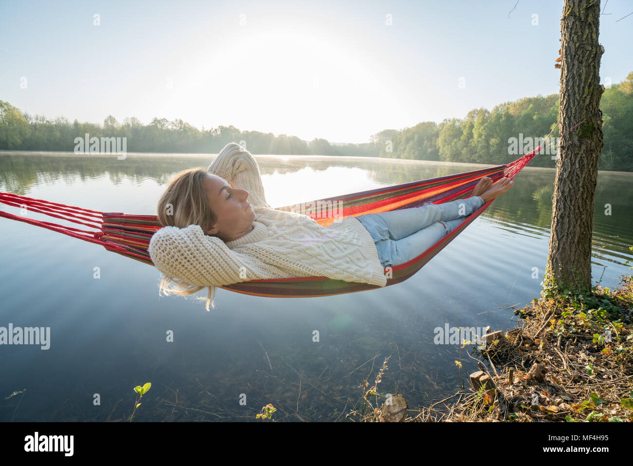 Young woman relaxing on hammock by the lake, la lumière du soleil et la réflexion. sunbeam Les gens bien-être détente dans la nature concept. France, Europe Banque D'Images