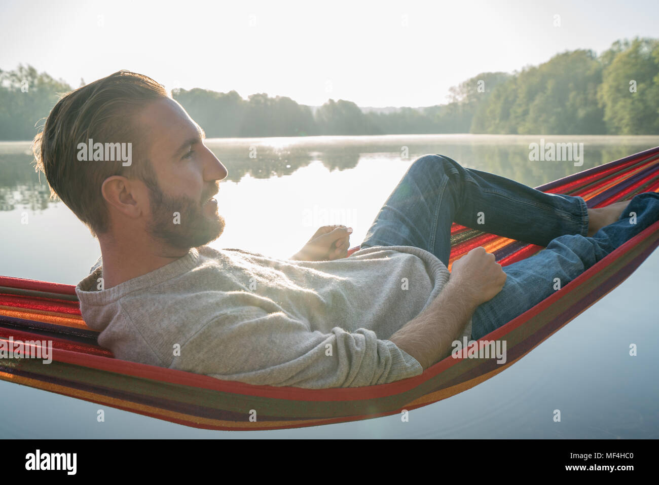Jeune homme sur hamac détente au bord de la lac dans le matin, la lumière du soleil. Les gens voyagent bien-être la paresse concept. France, Europe Banque D'Images