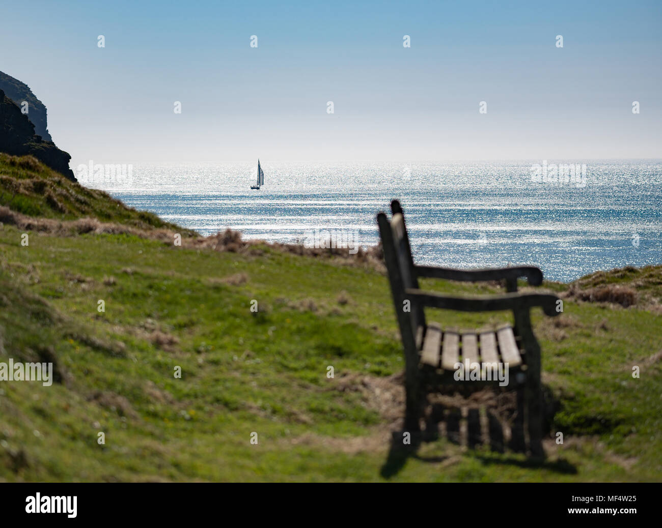 Banc public au son avec vue sur la mer et bateau à voile dans la distance Banque D'Images