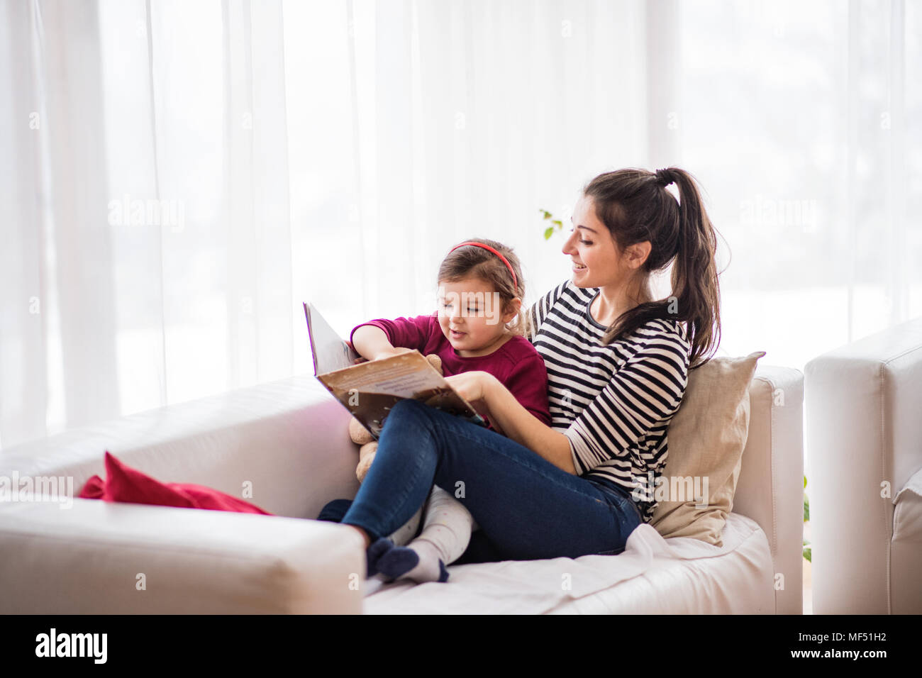 Jeune maman avec une petite fille à la maison, la lecture d'un livre. Banque D'Images