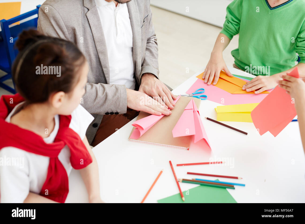 Des enfants avions en papier avec du papier de couleur pendant la leçon d'art alors qu'il était assis au bureau de classe avec l'enseignant Banque D'Images