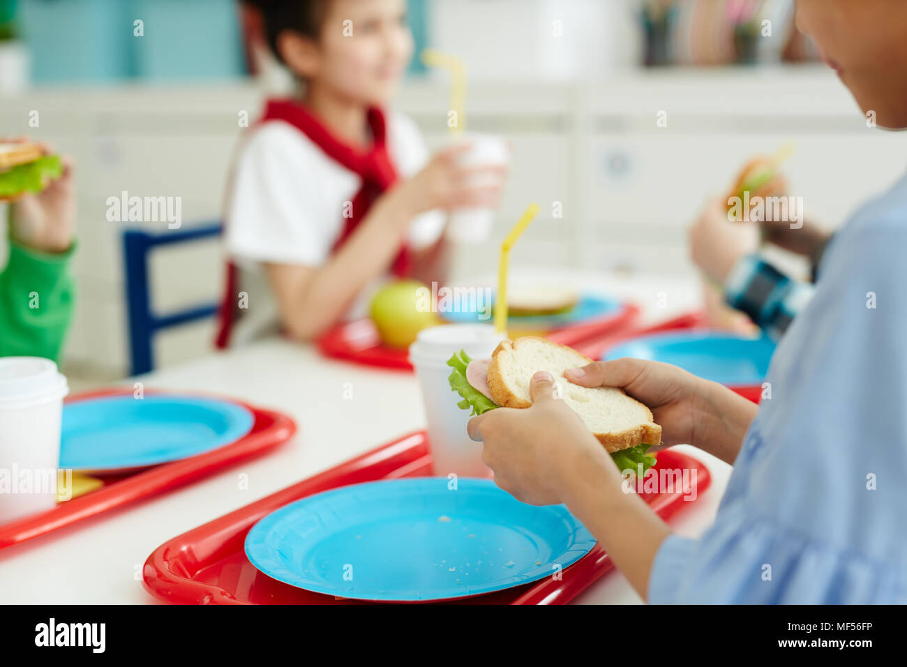 Enfants méconnaissables assis à table et de manger de savoureux sandwiches tout en déjeunant à la cantine de l'école élémentaire Banque D'Images