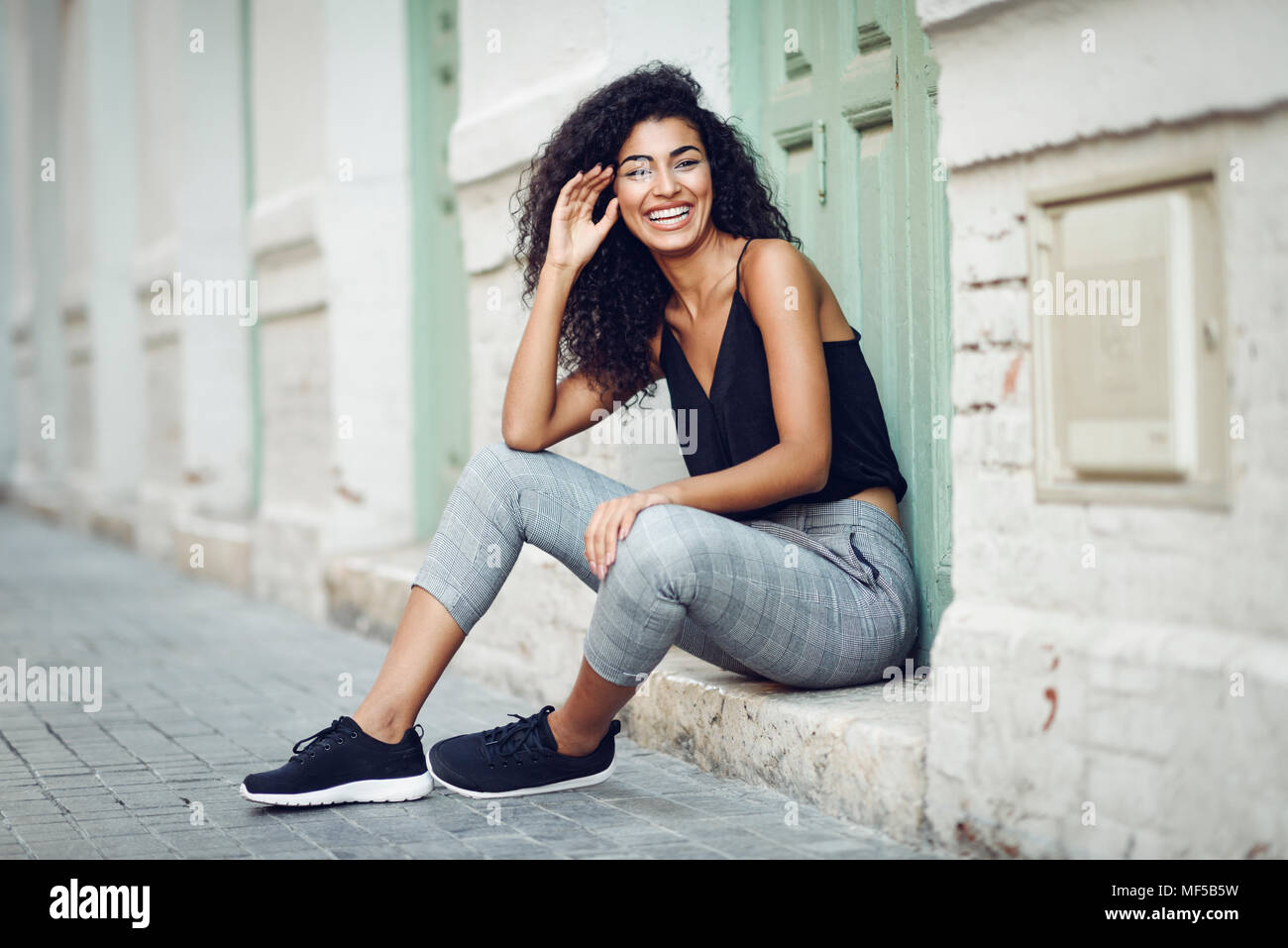 Portrait of laughing young woman sitting on l'étape devant une porte d'entrée Banque D'Images