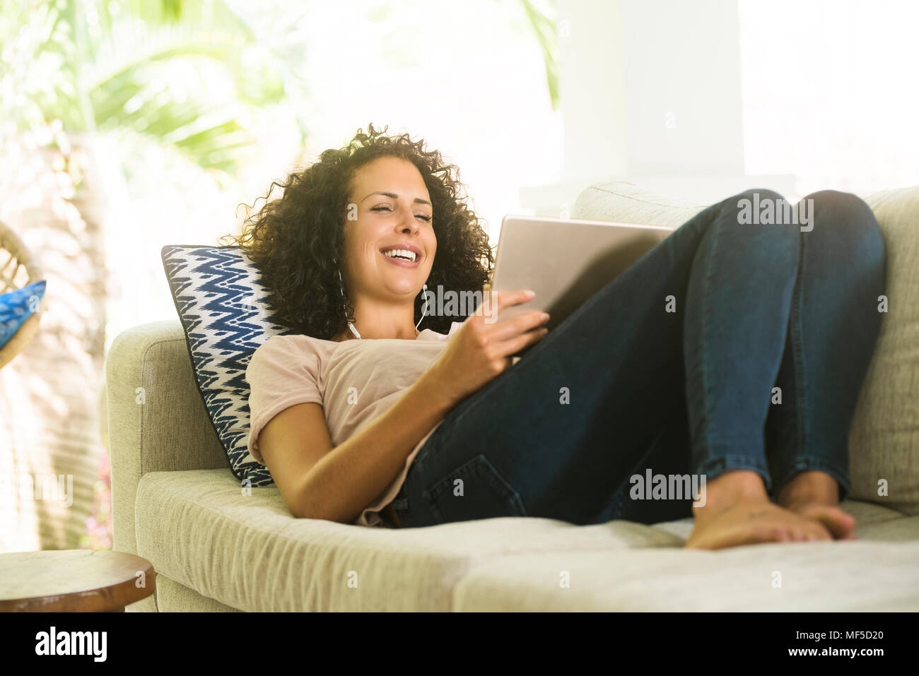 Happy woman lying on sofa with earphones et tablette Banque D'Images