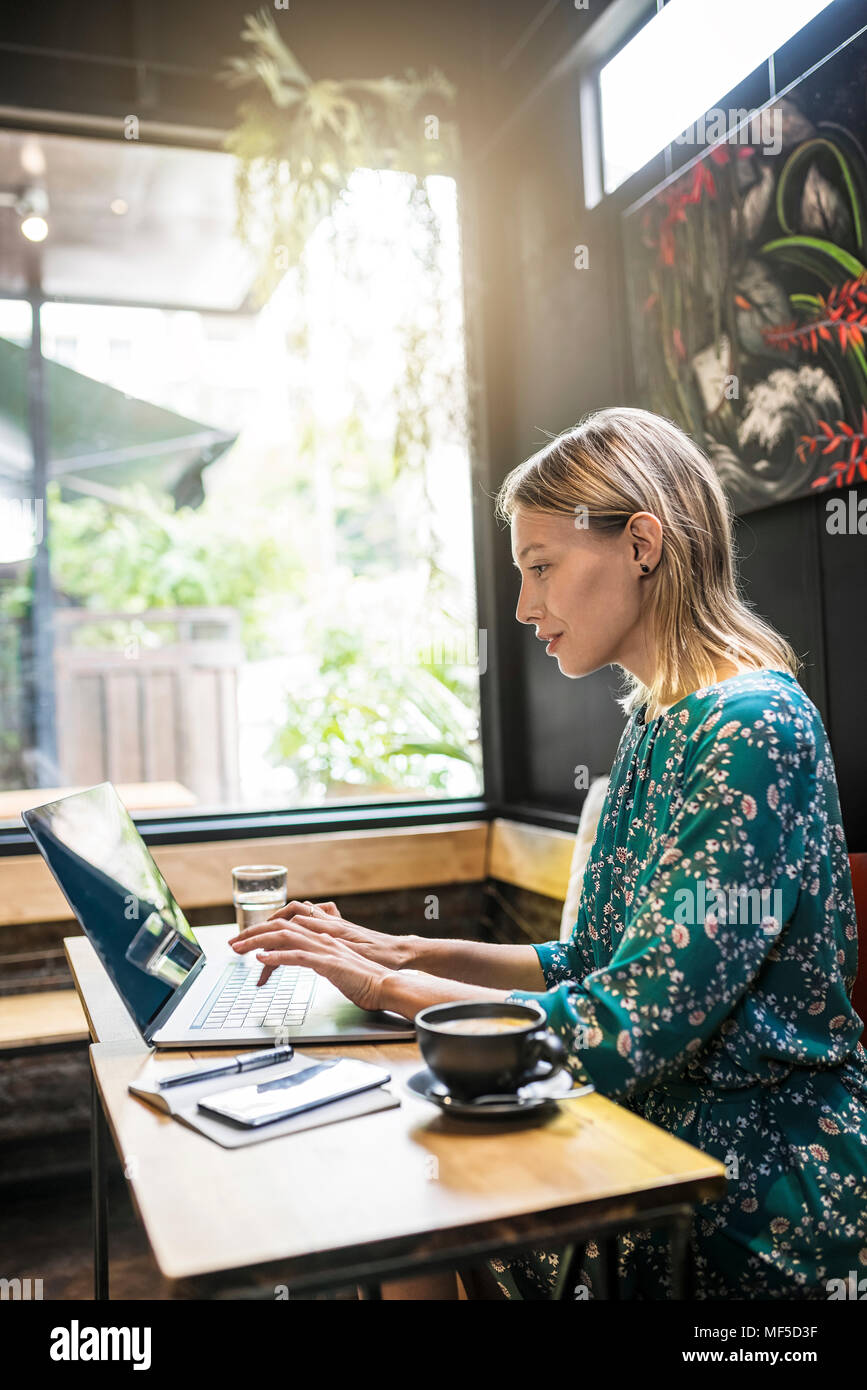 Jeune femme avec robe vert assis dans cafe , travailler sur son ordinateur portable Banque D'Images