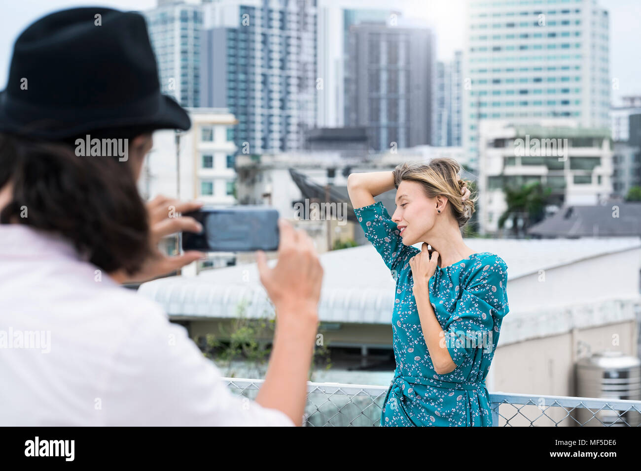 Homme TYoung avec smartphone prendre photo de copine posing on rooftop Banque D'Images