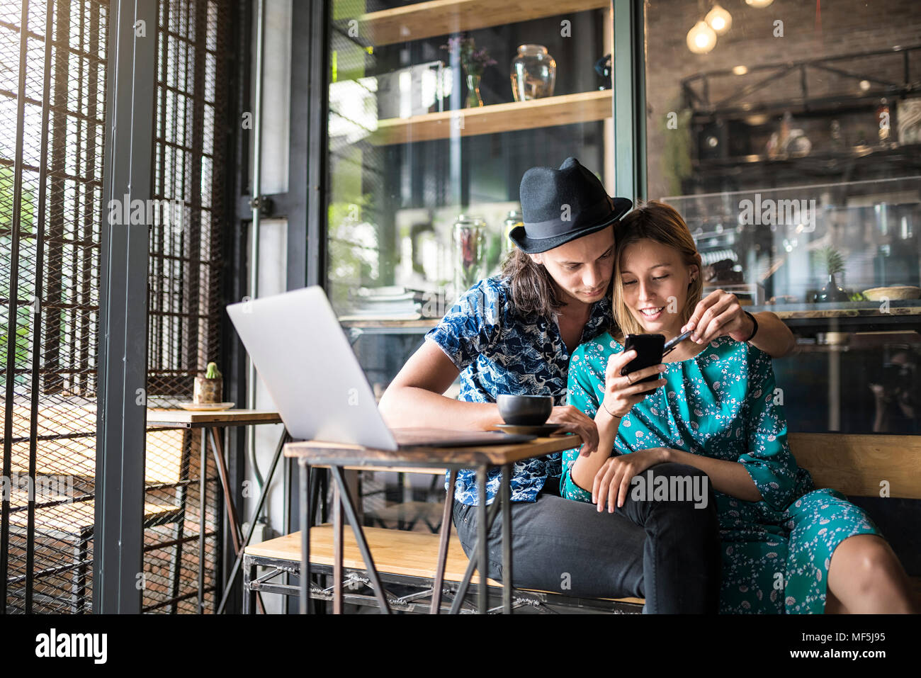 Artiste couple sitting in cafe et le contrôle de la jeune femme a smartphone Banque D'Images