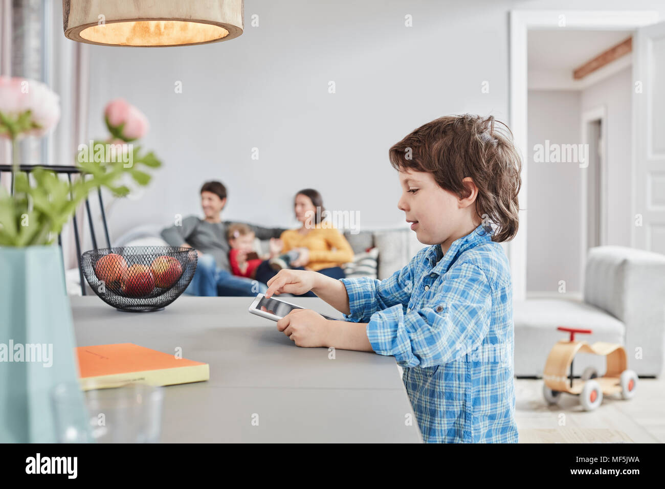 Boy looking at tablet à la maison avec la famille en arrière-plan Banque D'Images