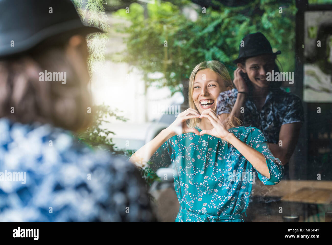 Belle jeune femme faisant un doigt frame heart et souriant à son petit ami au travers d'une fenêtre Banque D'Images