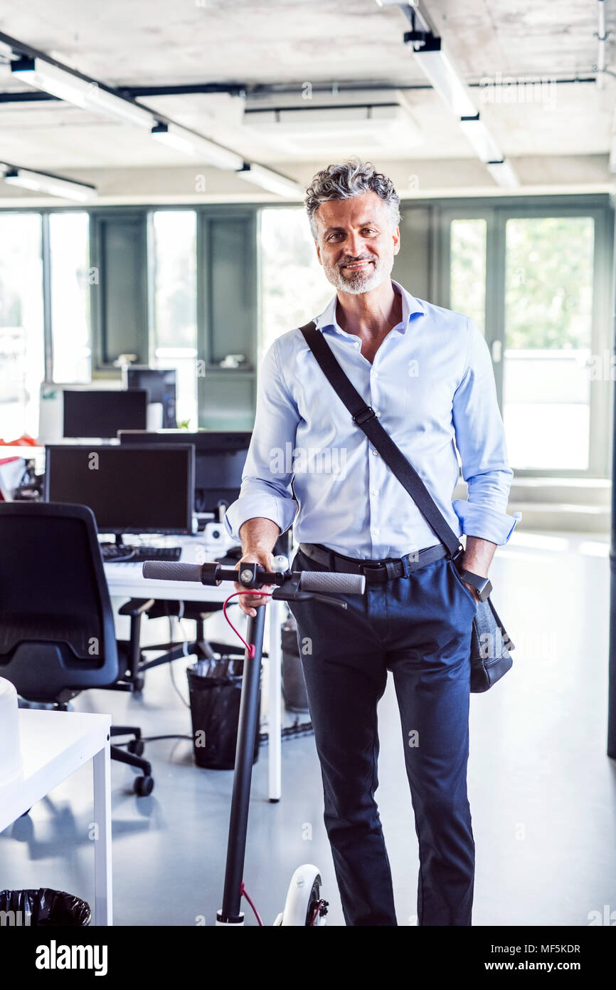 Portrait of smiling businesswoman with scooter in office Banque D'Images