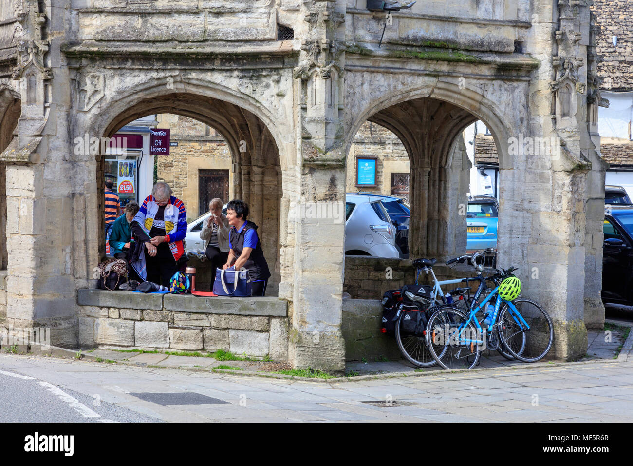 Les cyclistes et les visiteurs s'abriter du soleil chaud sur le marché Cross, Malmesbury, Wiltshire, Royaume-Uni Banque D'Images