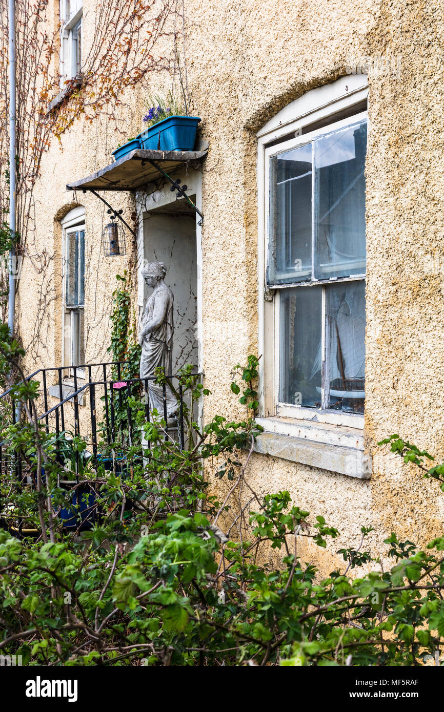 Une statue se dresse sur les étapes d'un cottage en décomposition sur Abbey Row, Malmesbury. Le jardin luxuriant et la décomposition sont étrangement attirant, Wiltshire, Royaume-Uni Banque D'Images