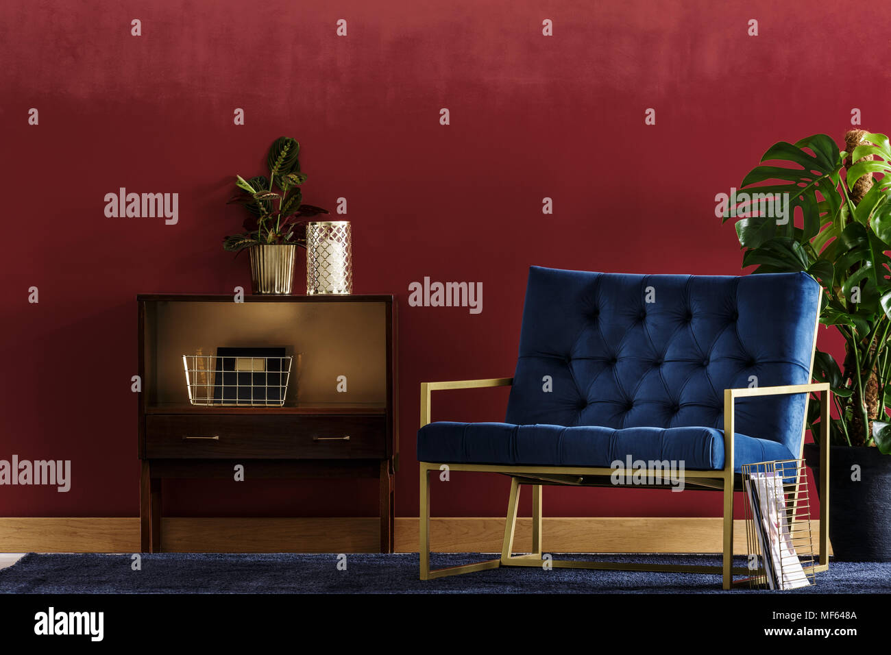 Petite armoire en bois, avec une usine et un fauteuil bleu marine debout dans un salon intérieur avec Monstera deliciosa Banque D'Images