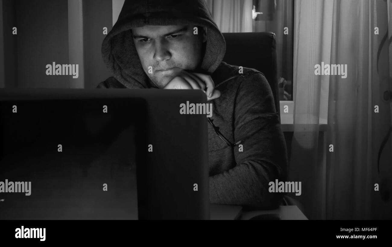 Le noir et blanc portrait of young man in hoodie working on laptop at night Banque D'Images
