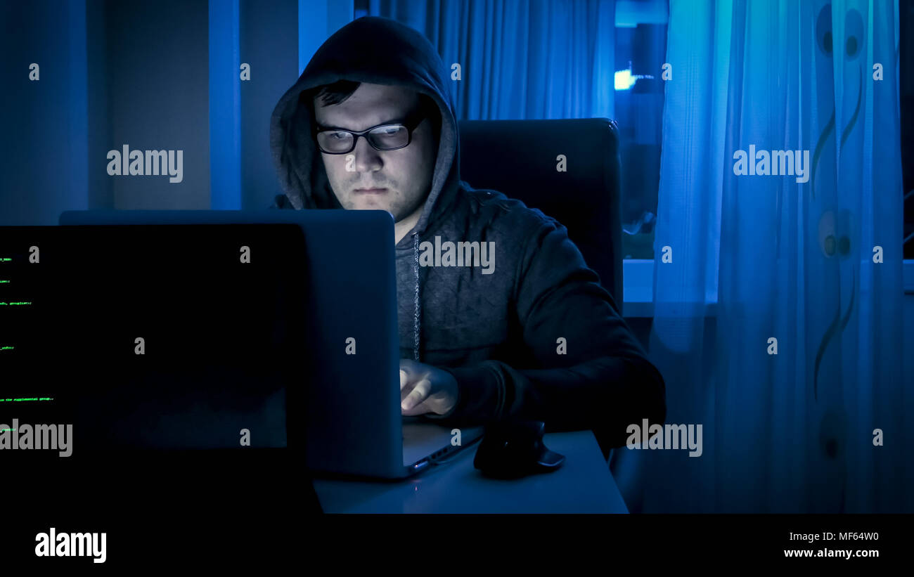 Jeune homme concentré dans les lunettes working on laptop at night Banque D'Images