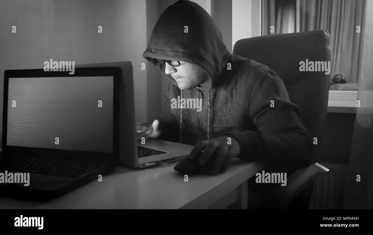 Portrait noir et blanc de jeunes hacker working on laptop at home Banque D'Images