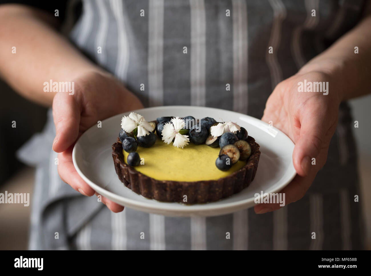 Mains tenant le citron et bleuets raw vegan gâteau décoré avec des fleurs comestibles Banque D'Images