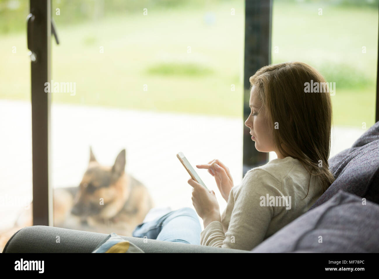Young woman relaxing on sofa using smartphone apps dans maison Banque D'Images