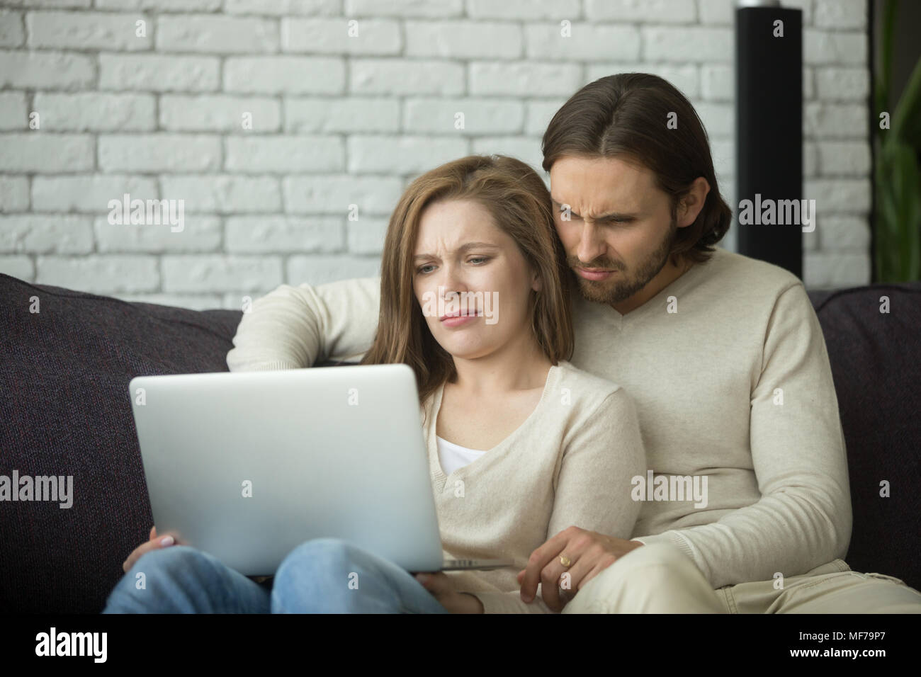 Jeune couple à la recherche sur l'ordinateur portable avec dégoût confus par news Banque D'Images