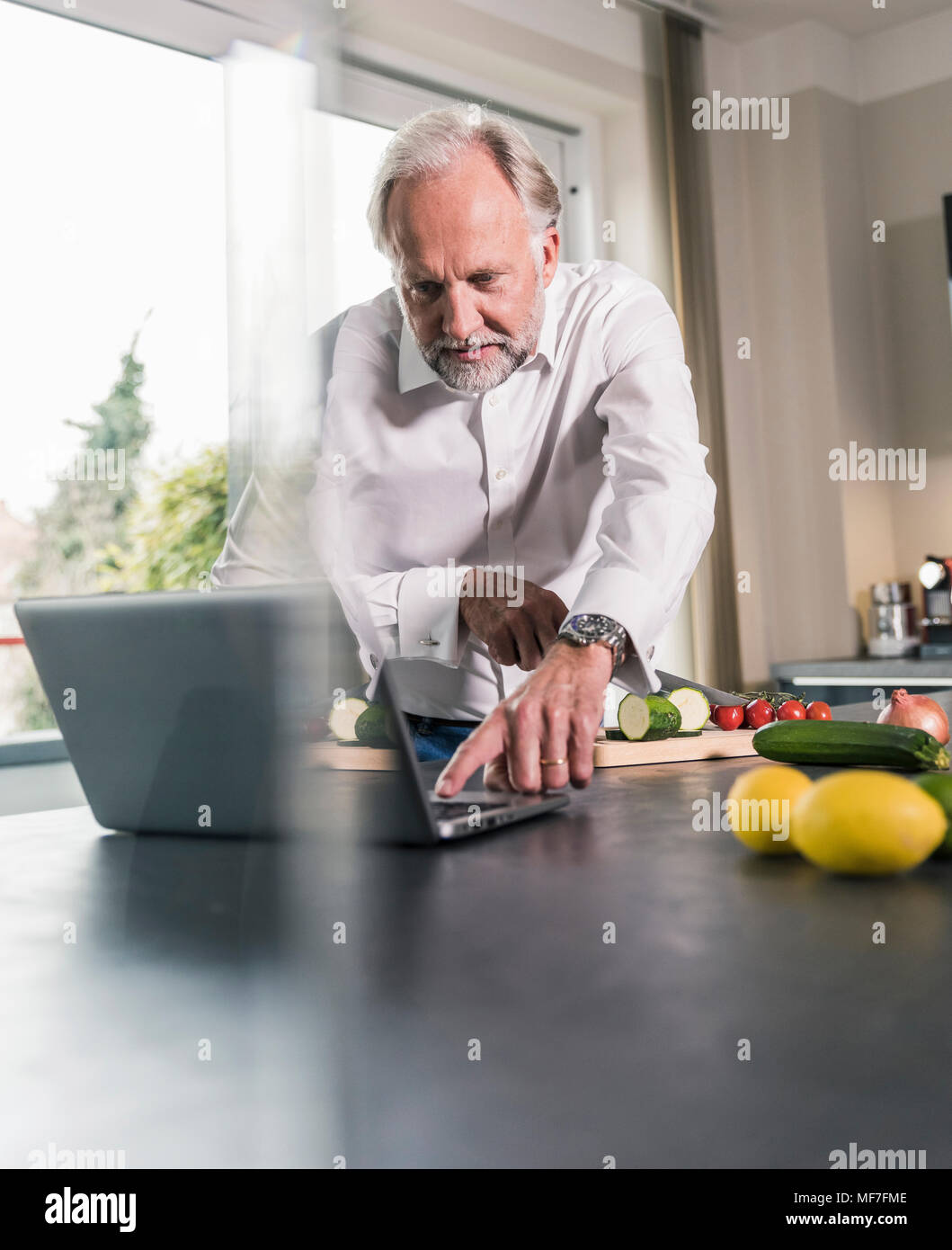 Homme mûr de préparer des aliments dans la cuisine pendant l'utilisation d'ordinateur portable Banque D'Images