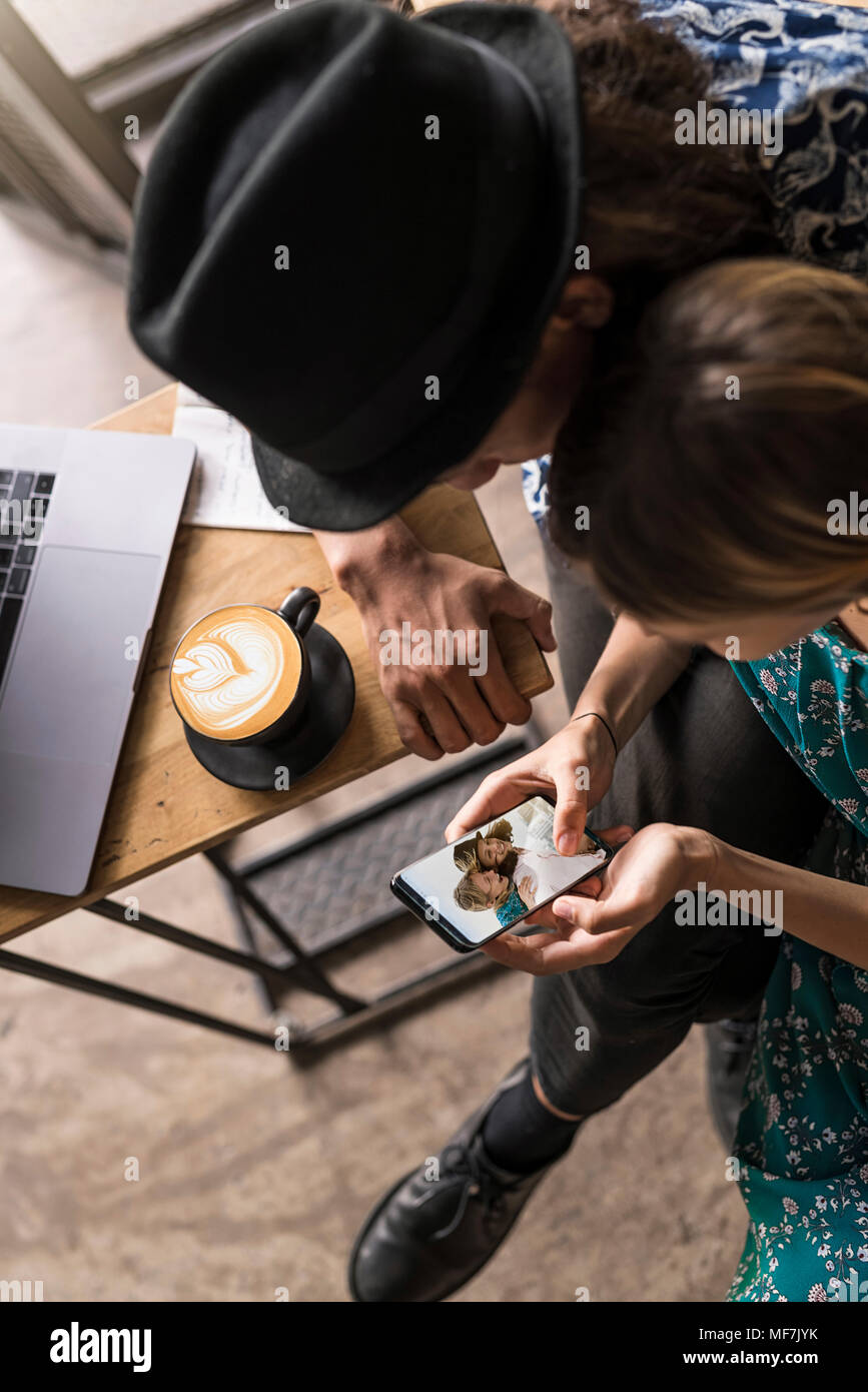 Artiste couple sitting in cafe et le contrôle de la jeune femme a smartphone Banque D'Images