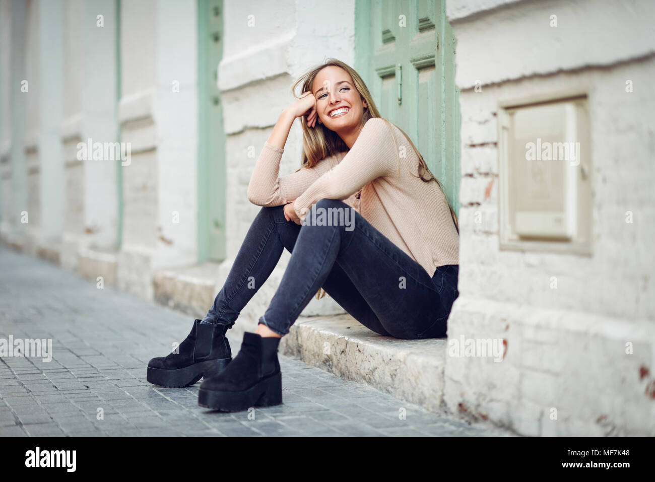 Rire jeune femme assise sur l'étape devant une porte d'entrée Banque D'Images