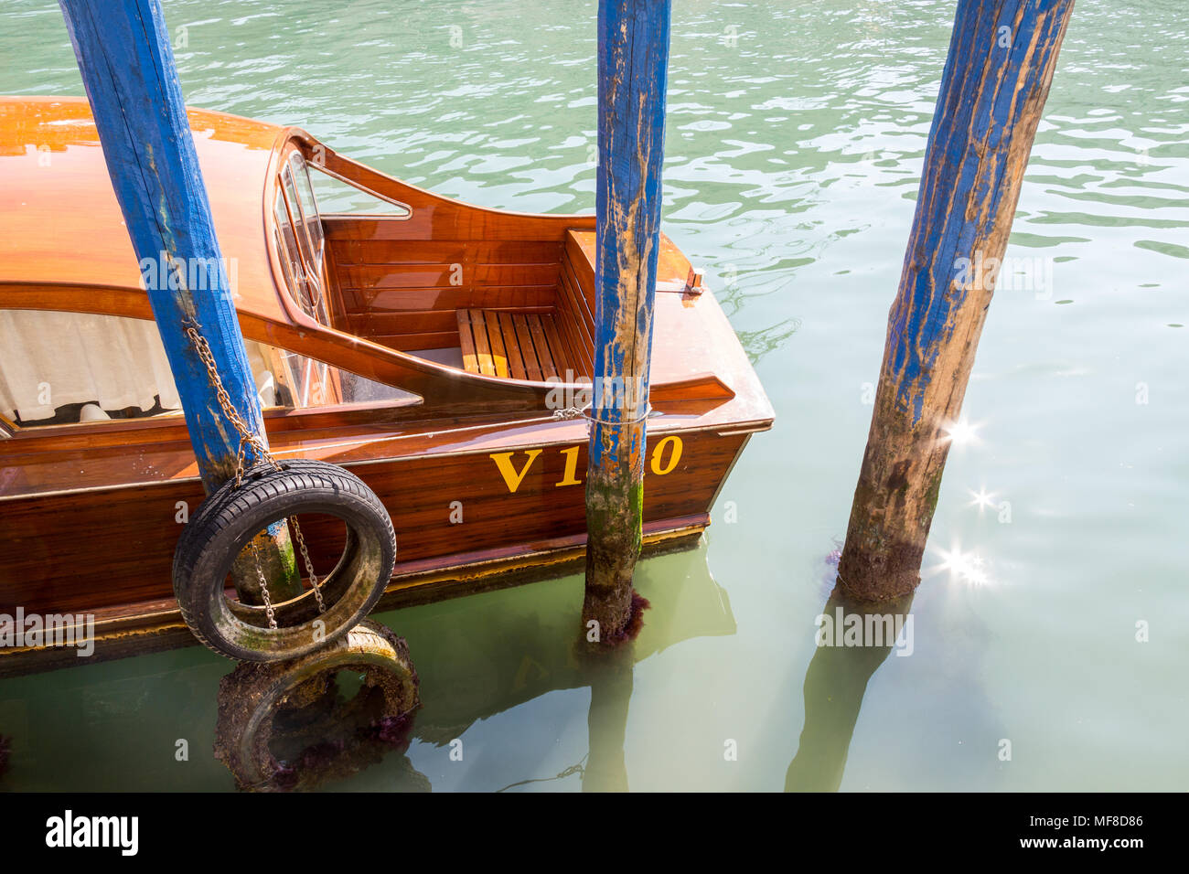Venise, Italie - 28 Février 2015 : un bateau de bois rouge lucious est mouillée sur des bollards bleu avec la Venise verte canal comme un backdro Banque D'Images