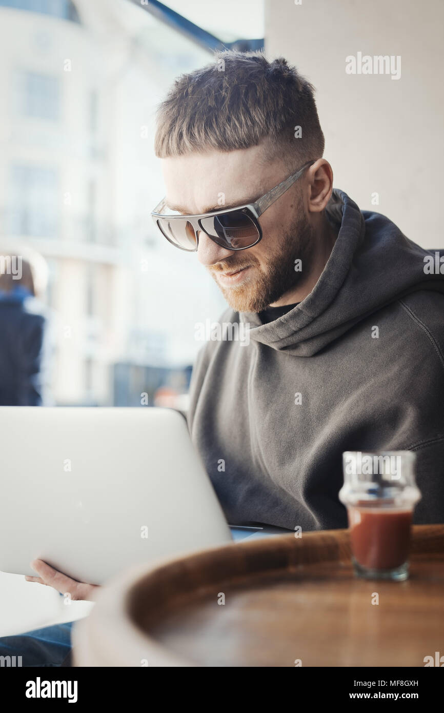 Pensive young man holding laptop sur les genoux et à y travailler dans le café. Banque D'Images