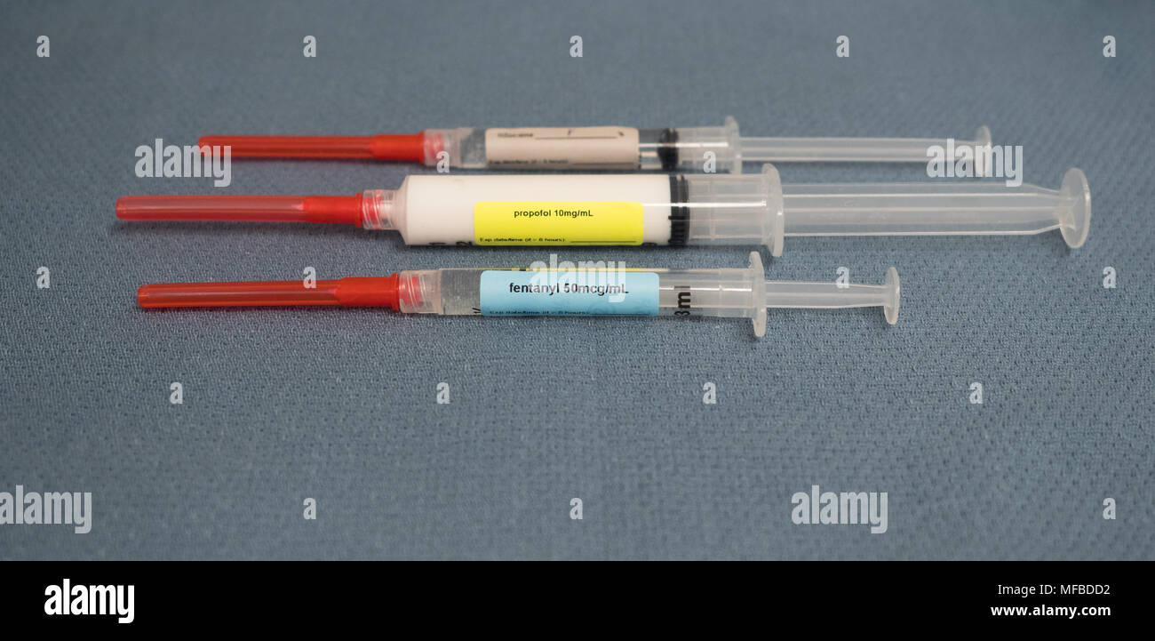 Trois seringues étiquetées avec les aiguilles de sécurité plafonné rouge contenant des médicaments utilisés pour l'anesthésie - le fentanyl, le propofol et de lidocaïne sur une serviette gris bleu. Banque D'Images