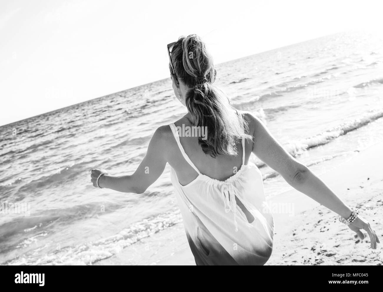 L'humeur joyeuse merveilleusement. Vus de derrière, jeune femme en robe sur la plage le soir balade Banque D'Images