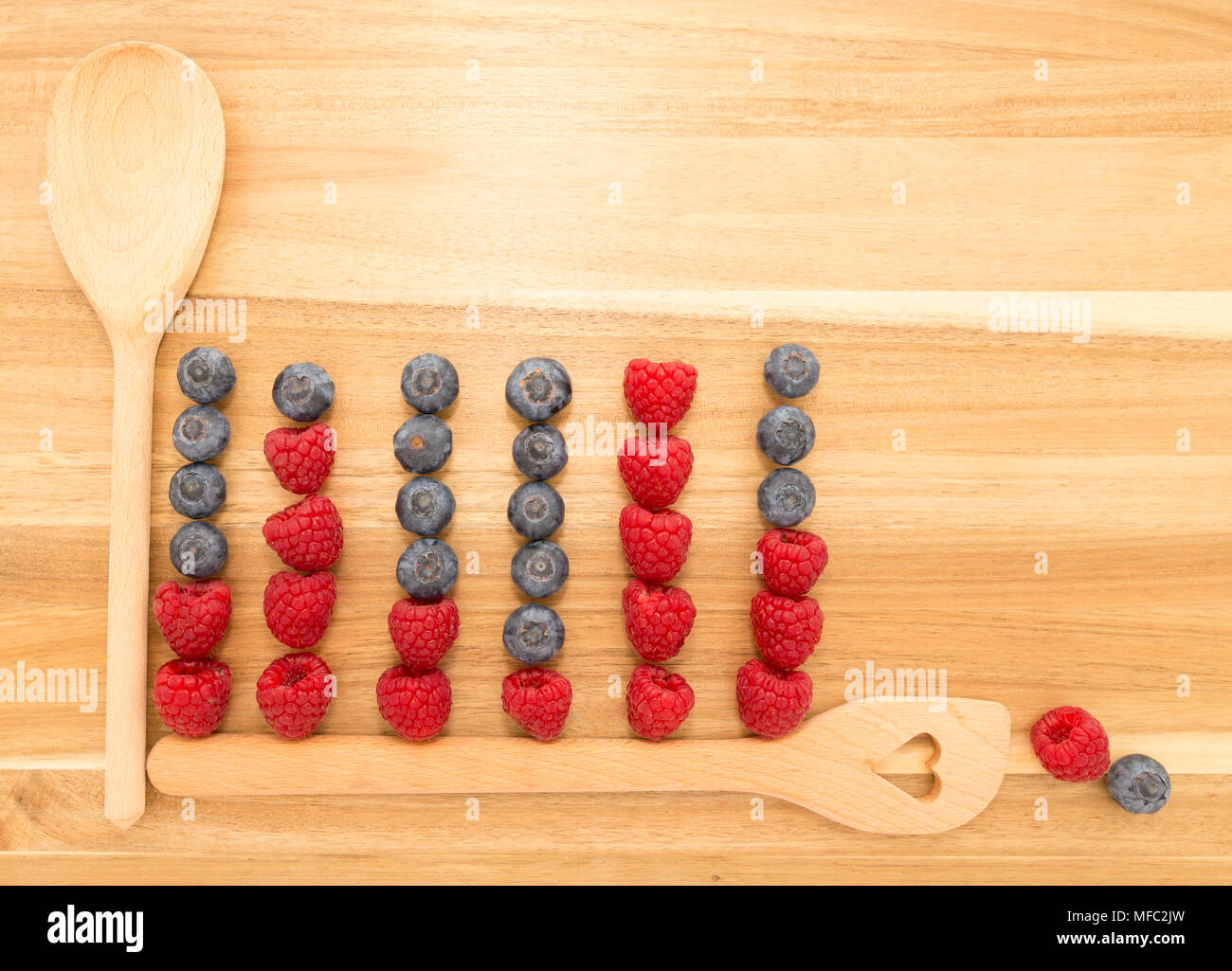 Graphique statistique faite de cuillères de cuisine, bleuets et framboises fraîches sur une planche à découper en bois brun Banque D'Images