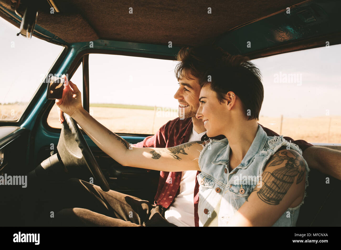 Cheerful young couple on a road trip profitant de la balade. L'homme et de la femme en prenant un sitting in car selfies. Banque D'Images