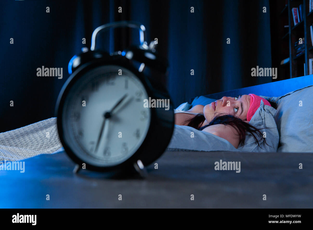 La photo d'une femme à l'insomnie avec bandage rose couché sur lit à côté de réveil Banque D'Images