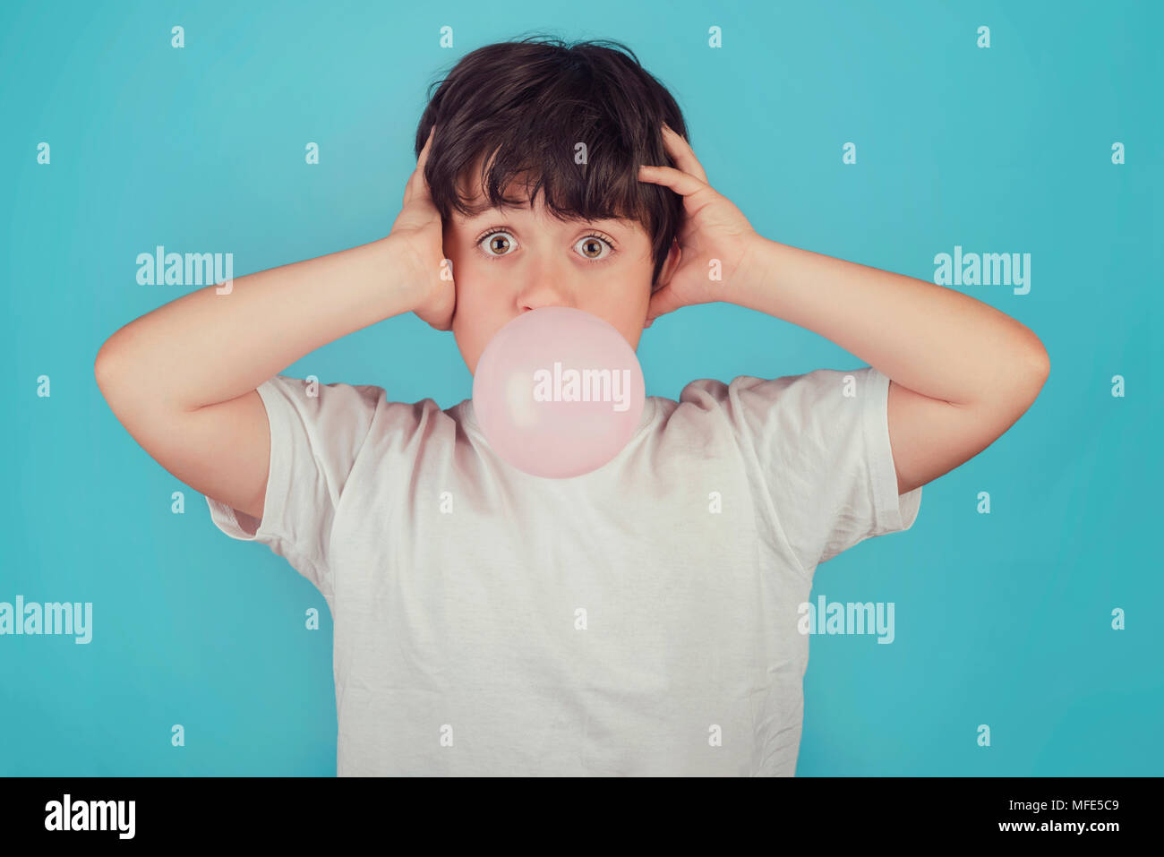 Enfant avec un chewing-gum dans la bouche sur fond bleu Banque D'Images