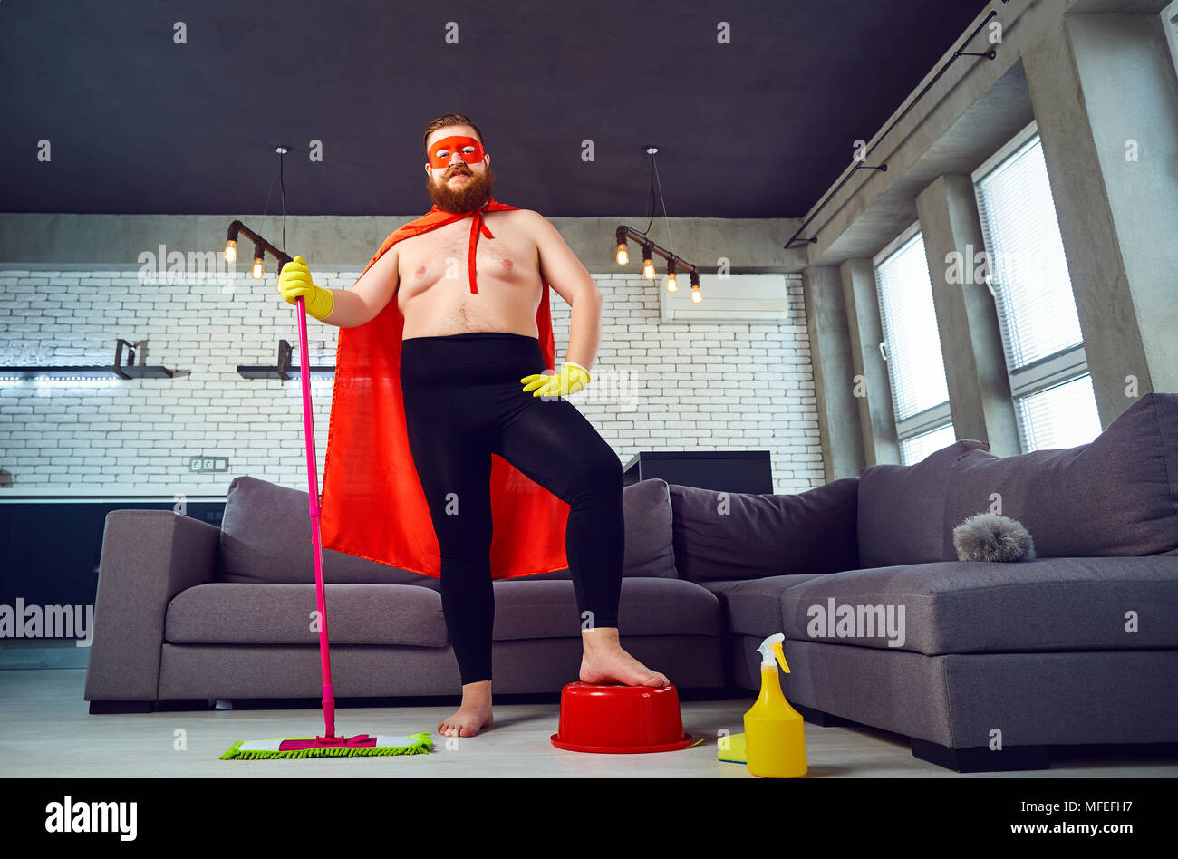 Une graisse, comique dans un costume de super-héro est le nettoyage de la chambre. Banque D'Images